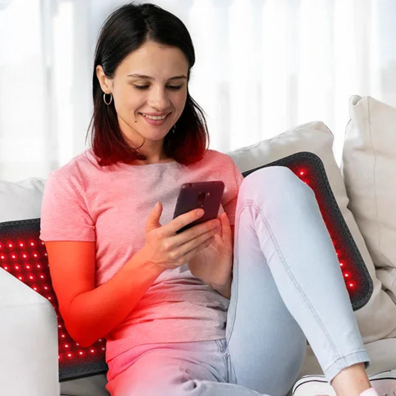 Woman using infrared light therapy seating on the sofa and reading her phone