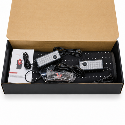 An open black gift box containing a infrared therapy mat with its accessories, including a power cord, plastic-wrapped parts, and a small instruction booklet, all set against a plain white background.
