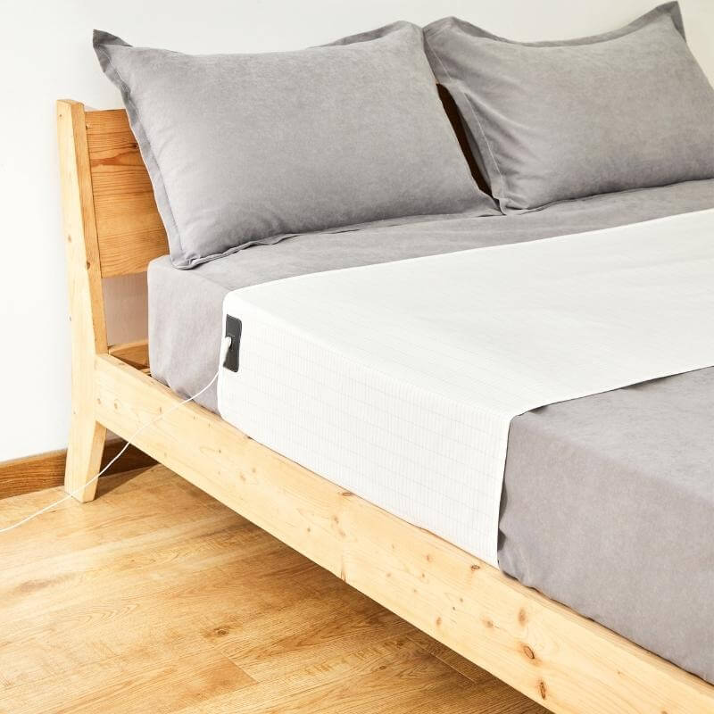 Wooden bed frame with gray bedding and pillows on a light wooden floor.