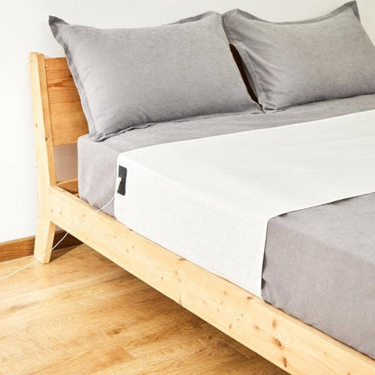 Wooden bed frame with gray bedding and pillows on a light wooden floor.