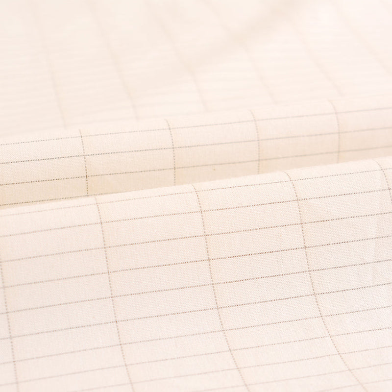 A close-up of a beige-colored fabric with a silver fibre, light brown grid pattern, shown with soft folds.