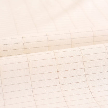 A close-up of a beige-colored fabric with a silver fibre, light brown grid pattern, shown with soft folds.